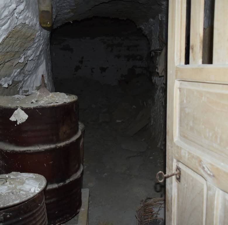 Cave house entrance in Benamaurel, Granada, with barrels and wooden door.