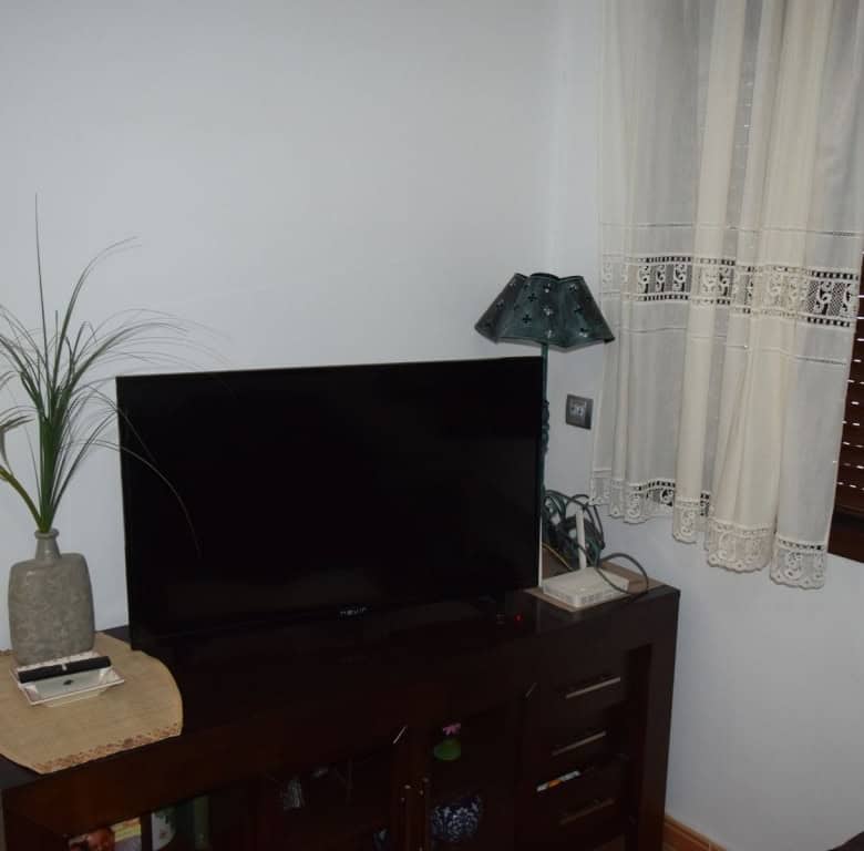 Interior view of a cave house in Freila, Granada with a TV, wooden furniture, and window with curtai.