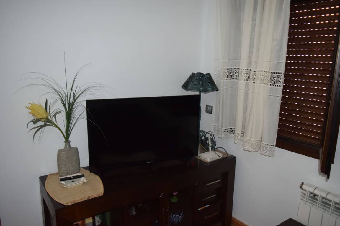 Interior view of a cave house in Freila, Granada with a TV, wooden furniture, and window with curtai.