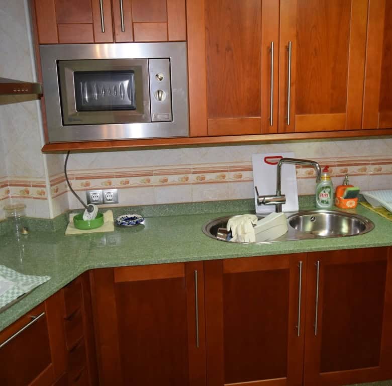 Cave house kitchen with wooden cabinets, microwave, sink, and green countertop in Freila, Granada.