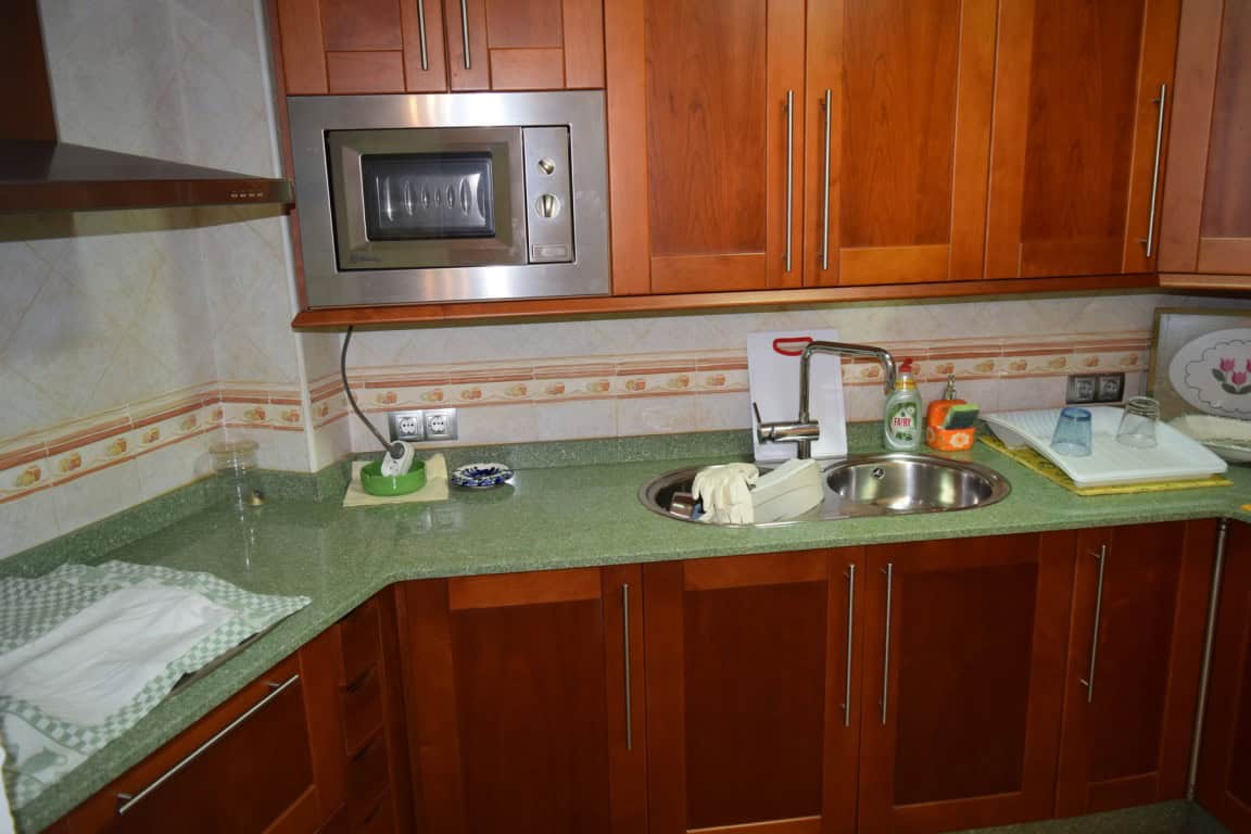 Cave house kitchen with wooden cabinets, microwave, sink, and green countertop in Freila, Granada.