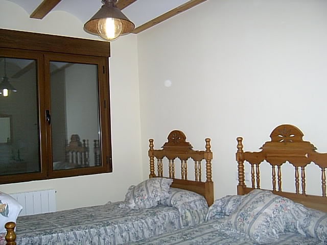 Cozy bedroom with two wooden beds in a rustic finca in Huescar, Granada, featuring traditional decor.