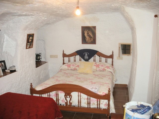 Unique cave house interior in Benamaurel, Granada, featuring rustic wooden bed and cozy decor.