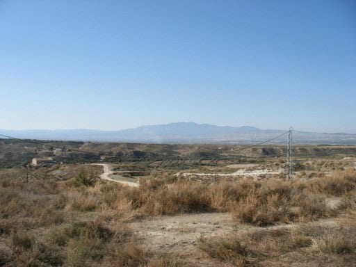 Ancient ruin in Benamaurel, Granada, with open landscape and distant mountains under a clear blue sk.