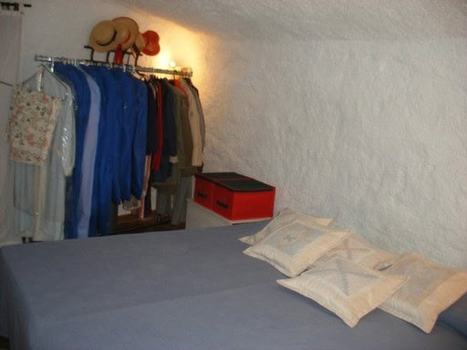 Cave house bedroom with bed, pillows, and clothing storage in Cortes de Baza, Granada.