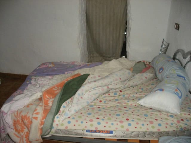 Cozy bedroom inside a cave house in Cuevas del Campo, Granada, featuring a simple bed with colorful.