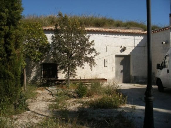 Cave house in Castillejar, Granada, with white exterior walls, surrounded by greenery and a clear bl.