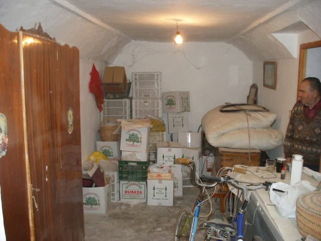 Cave house interior in Castillejar, Granada, with storage boxes, furniture, and a person standing in.