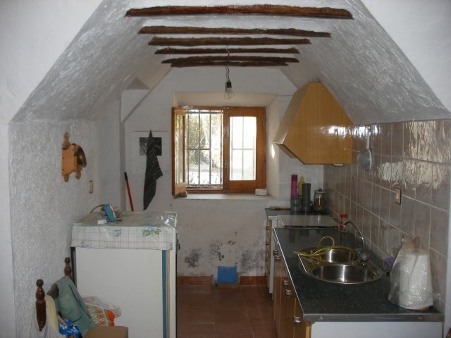 Charming cave house kitchen with rustic wooden beams and a small window in Castillejar, Granada.