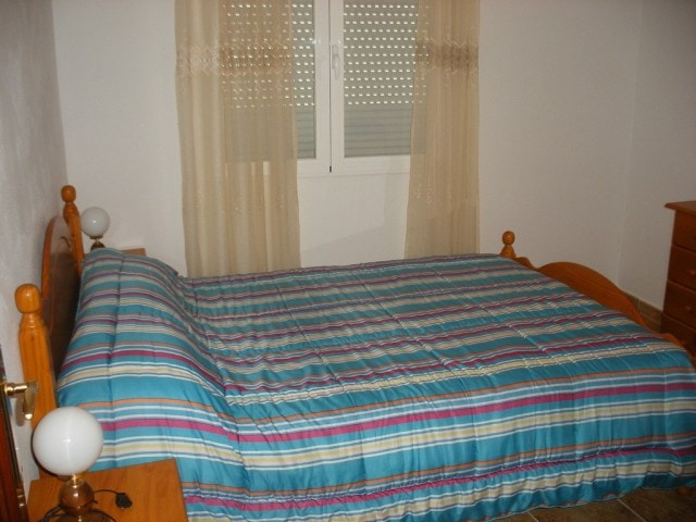 Bedroom with wooden bed frame and colorful striped bedding in Castillejar, Granada.