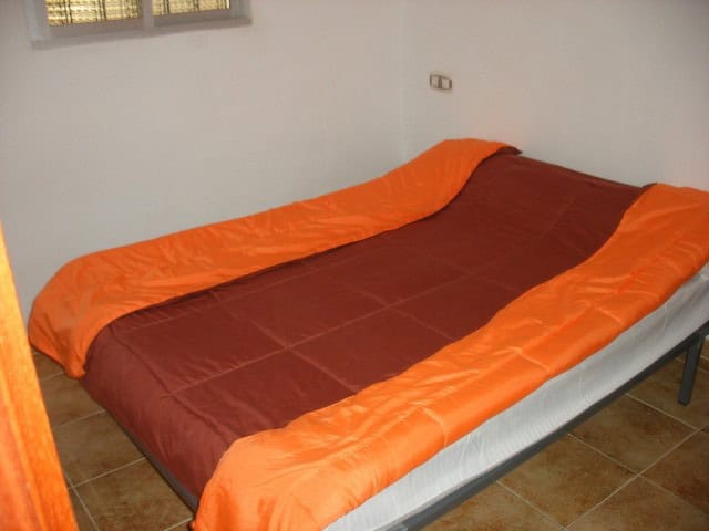 Double bed with orange and brown bedding in a simple bedroom setting.