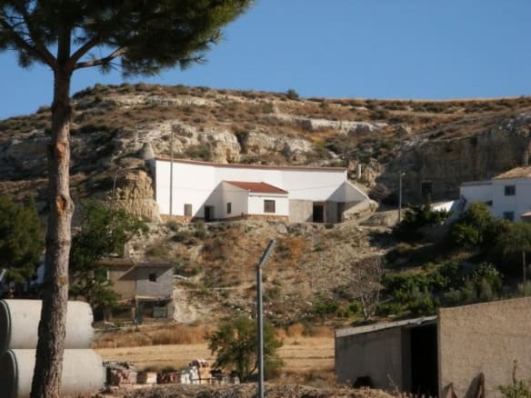 Cave house nestled in Cuevas del Campo, Granada, with white exterior and scenic hillside views.