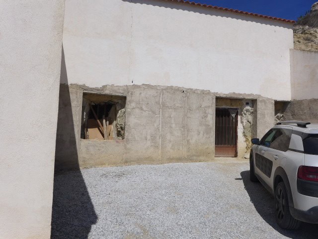 Cave house exterior in Cuevas del Campo, Granada, with a car parked outside and a simple entrance.