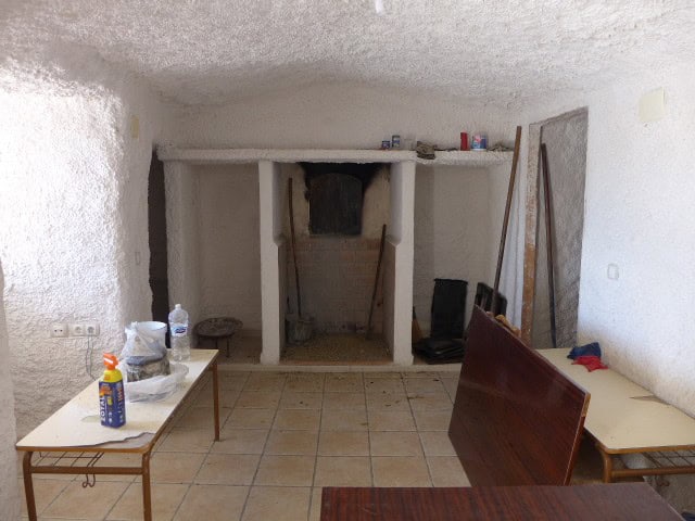 Interior view of a traditional cave house in Cuevas del Campo, Granada, showing rustic walls and sim.