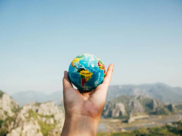 Hand holding a small globe with a landscape background, symbolizing international property buying.