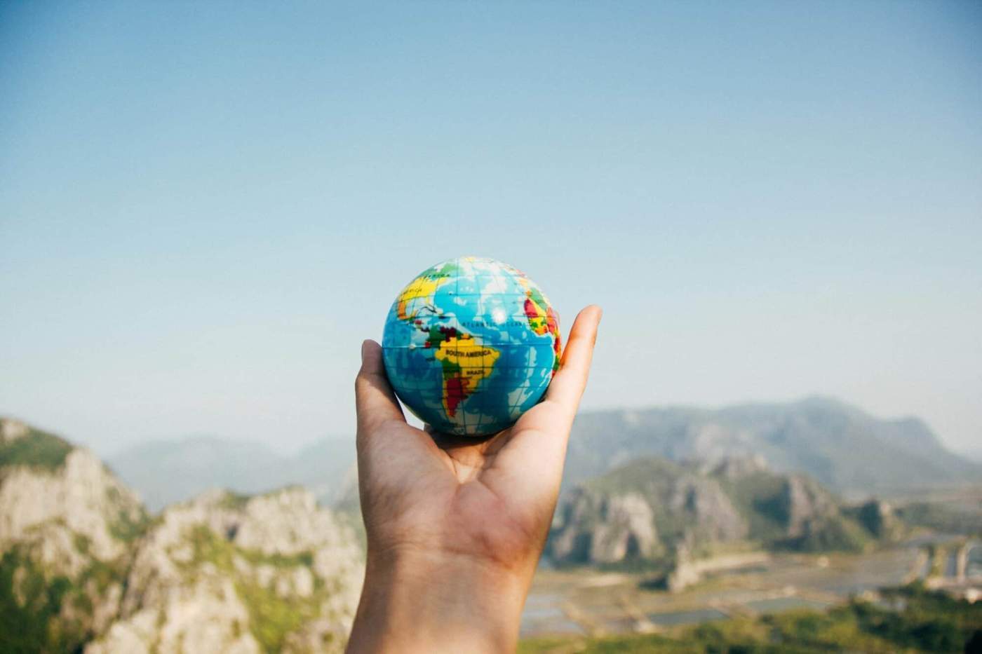 Hand holding a small globe with a landscape background, symbolizing international property buying.