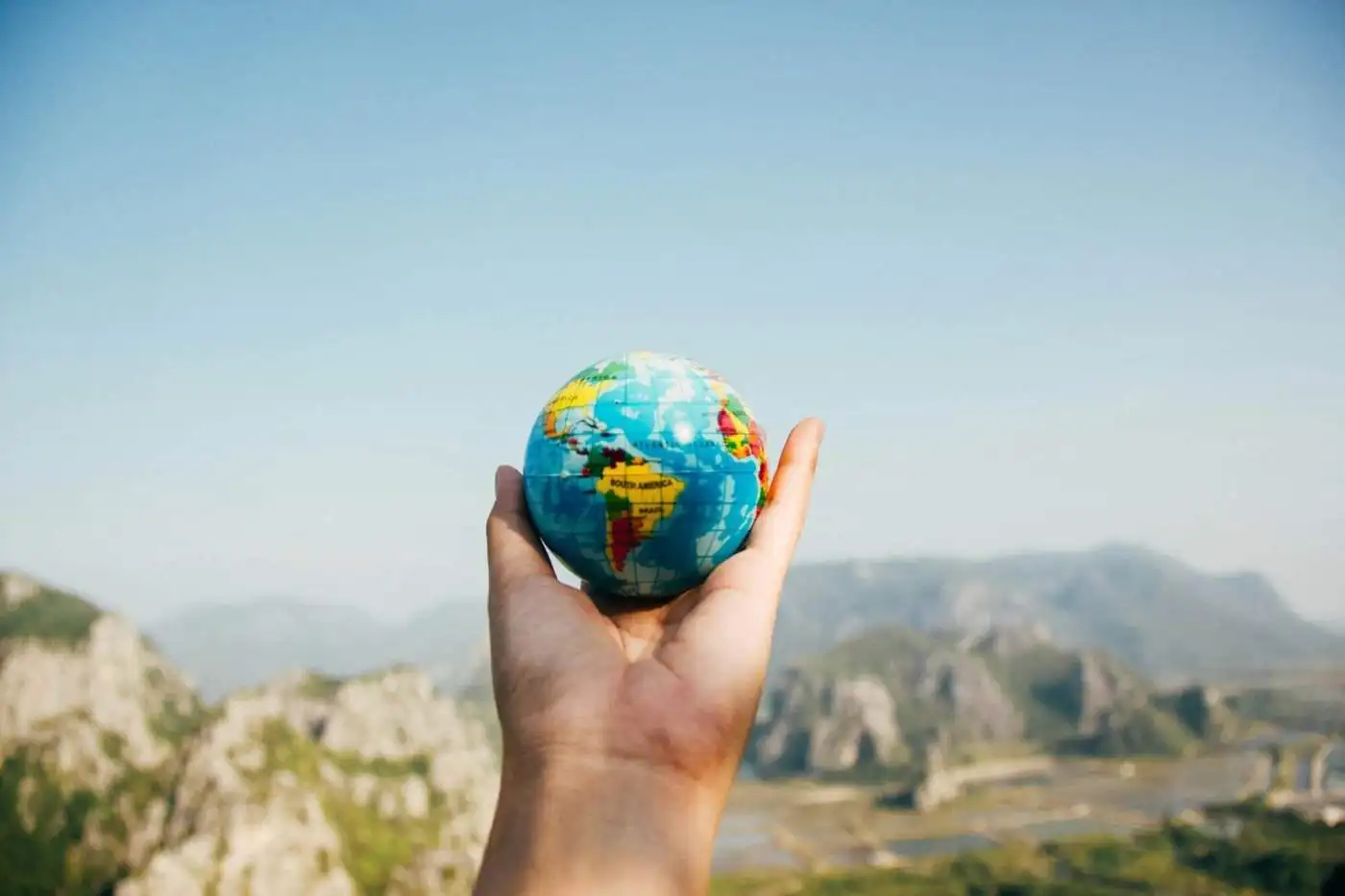 Hand holding a small globe with a landscape background, symbolizing international property buying.