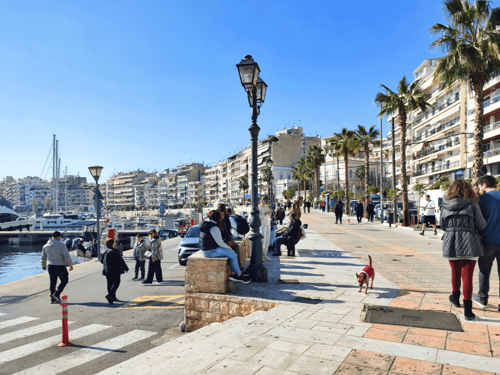 Athens waterfront promenade with palm trees, benches, and people enjoying the sunny day.
