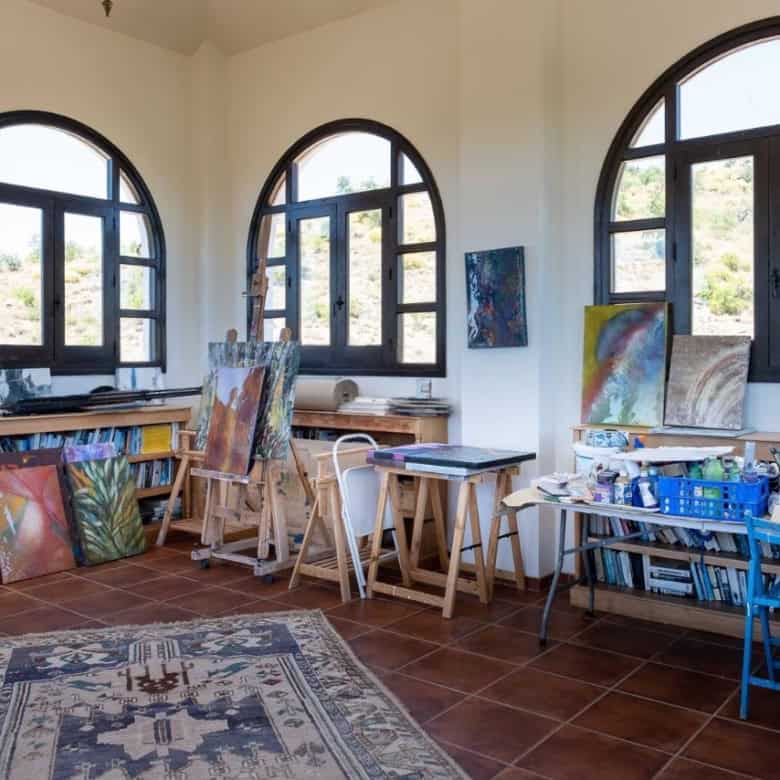 Bright art studio featuring large arched windows, easels, and painting supplies for creative work.