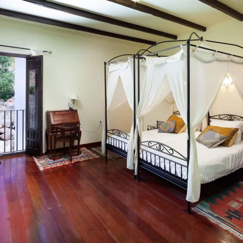 Cozy bedroom featuring a stylish canopy bed, wooden floors, and natural light from the balcony. Perf.