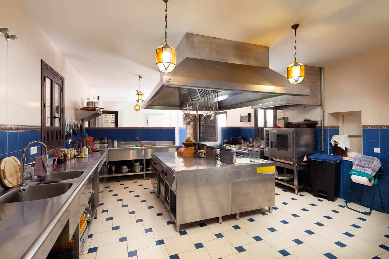 Commercial kitchen with stainless steel appliances and blue tiled walls.