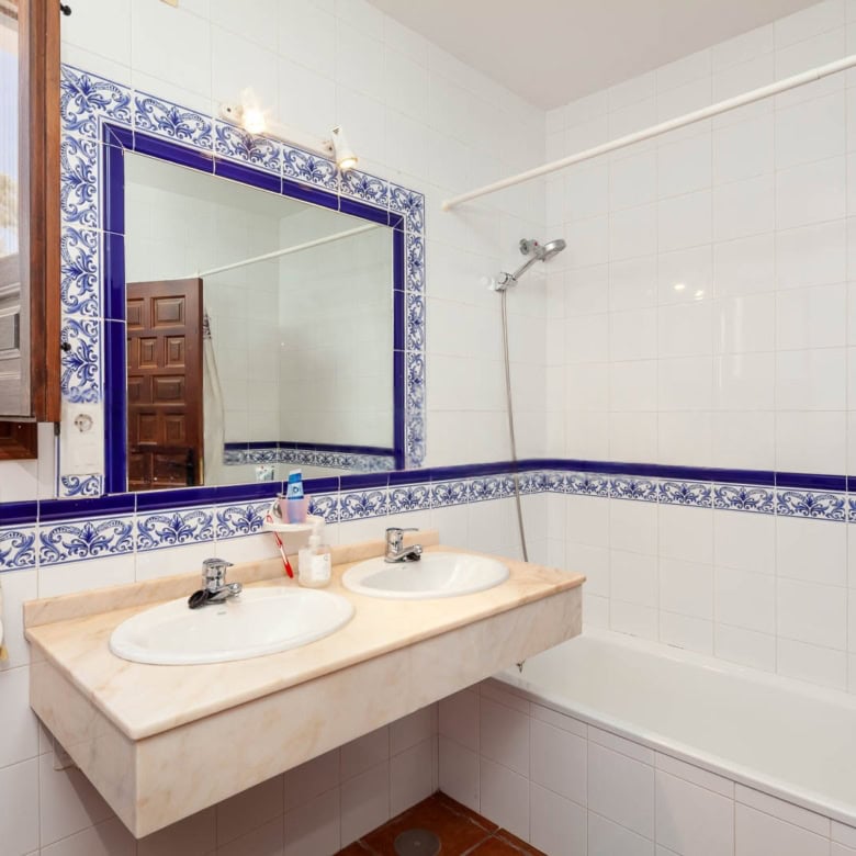 Bathroom with dual sinks, large mirror, and white tiled walls with blue decorative border.
