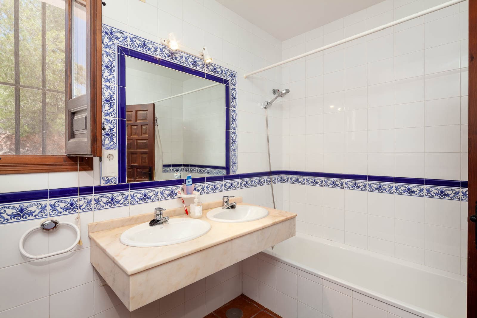 Bathroom with dual sinks, large mirror, and white tiled walls with blue decorative border.