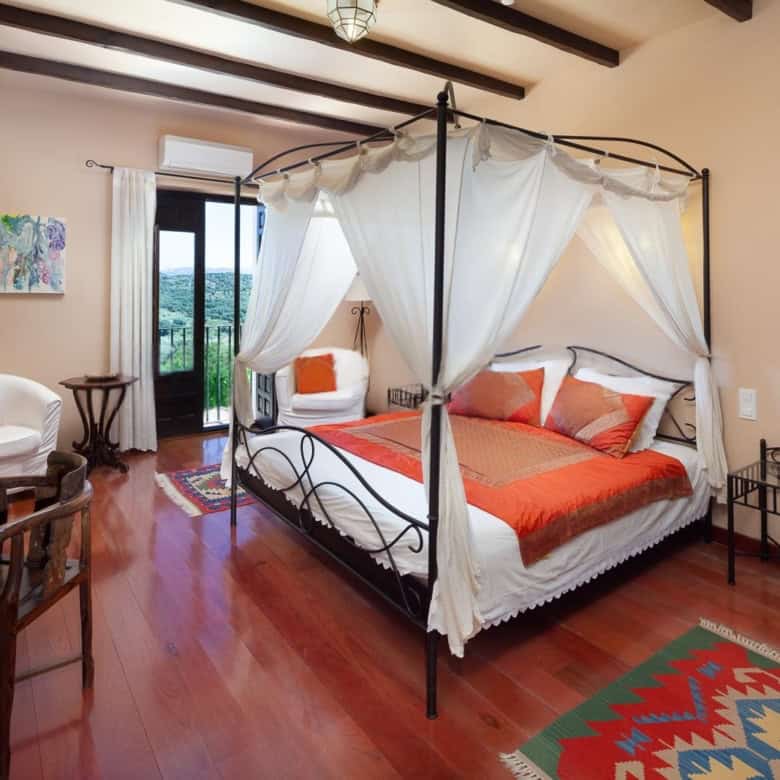 Elegant bedroom featuring a four-poster canopy bed with white drapes and vibrant orange bedding.
