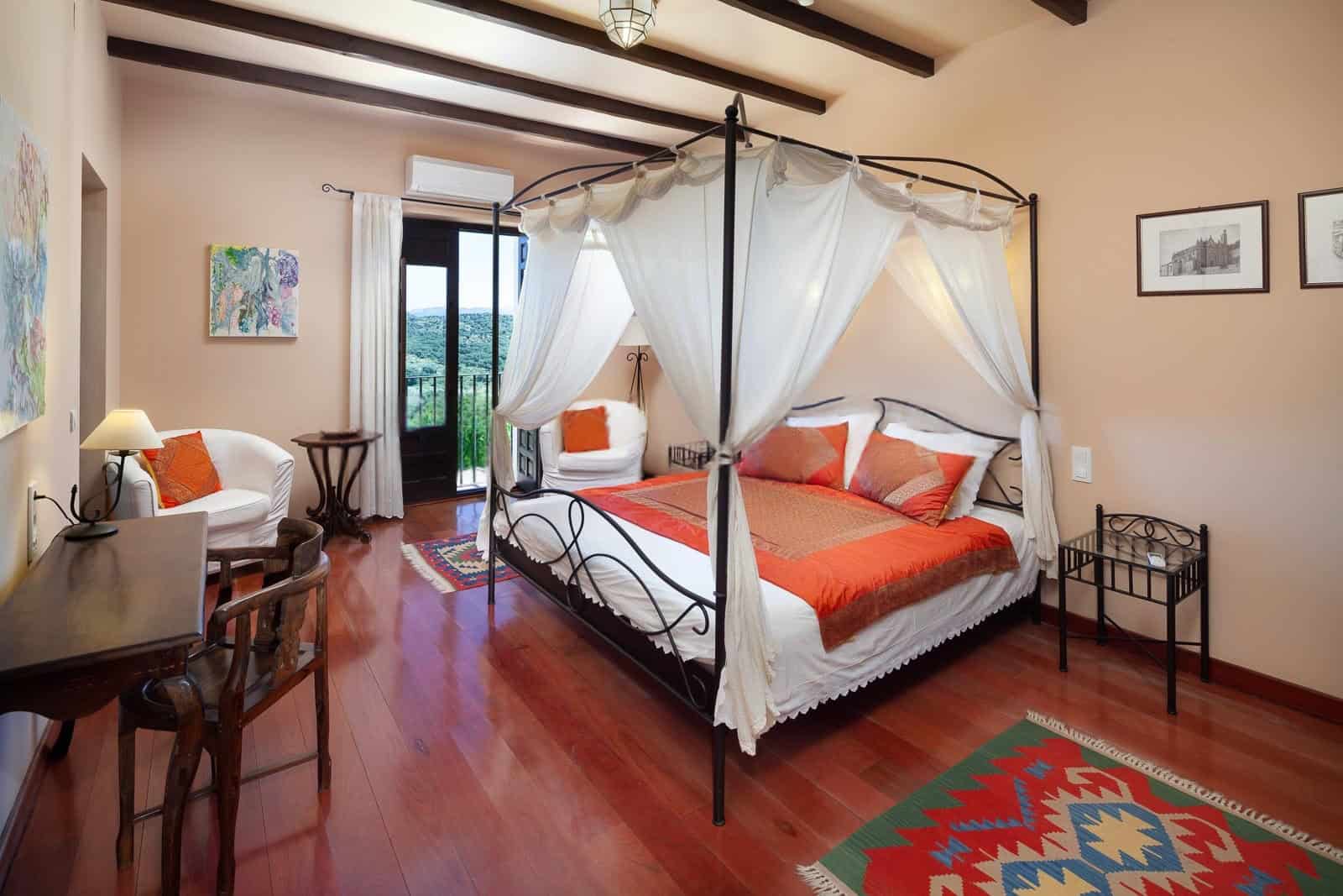 Elegant bedroom featuring a four-poster canopy bed with white drapes and vibrant orange bedding.