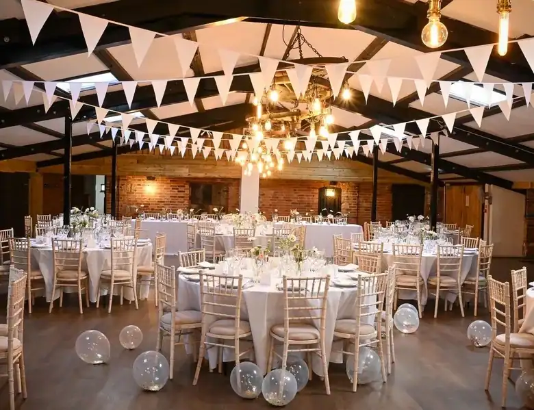 Elegant wedding reception with round tables, white chairs, and festive decorations in a stylish venu.