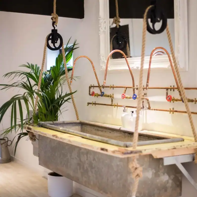 Vintage industrial laundry sink with copper pipes and hanging ropes in a stylish home.