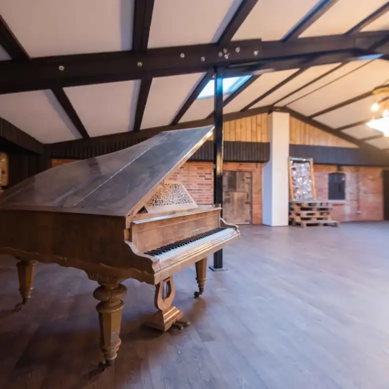 Grand piano on wooden floor in large, stylish event space with brick walls and modern lighting.
