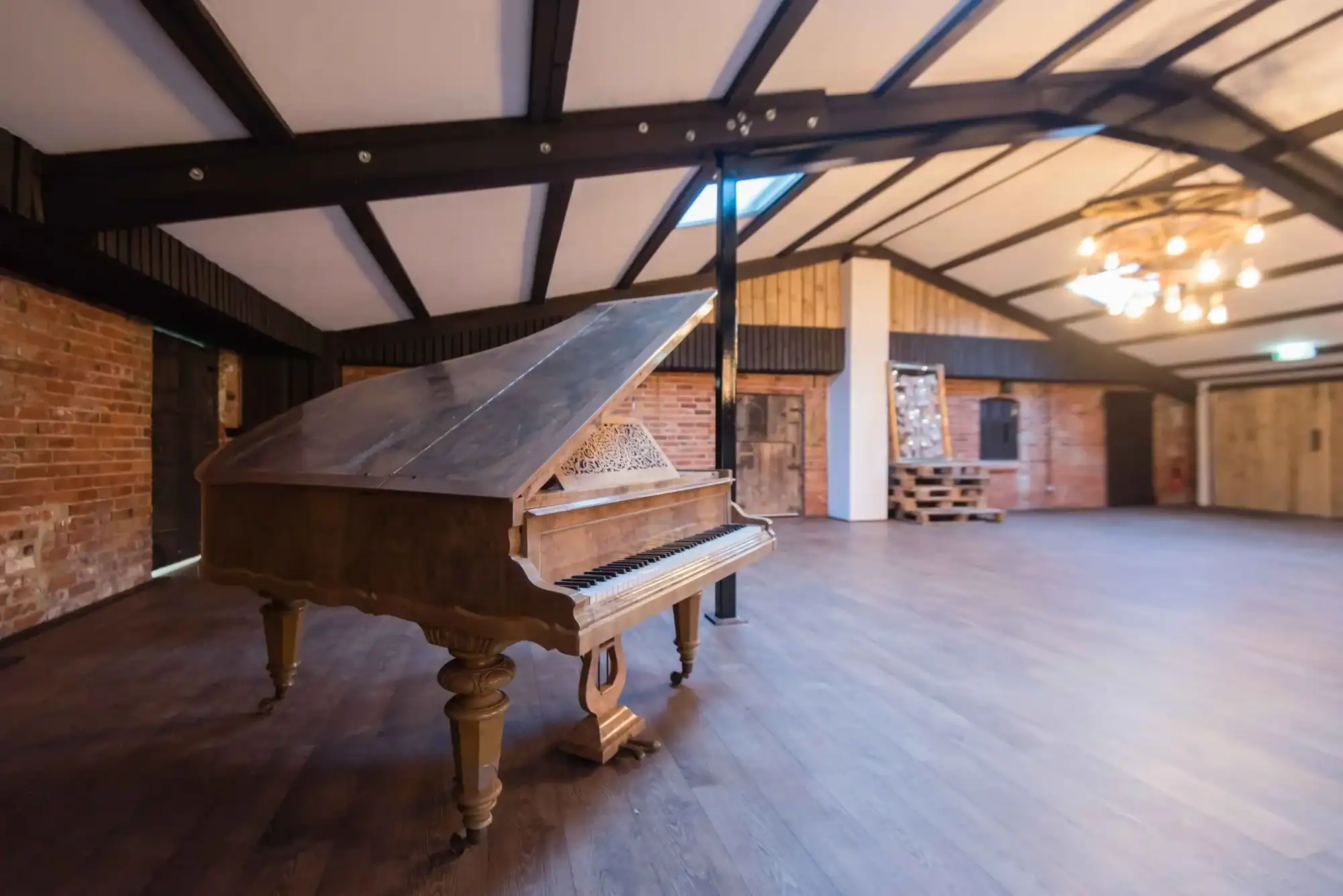 Grand Piano in Spacious Event Hall Grand piano on wooden floor in large, stylish event space with brick walls and modern lighting.