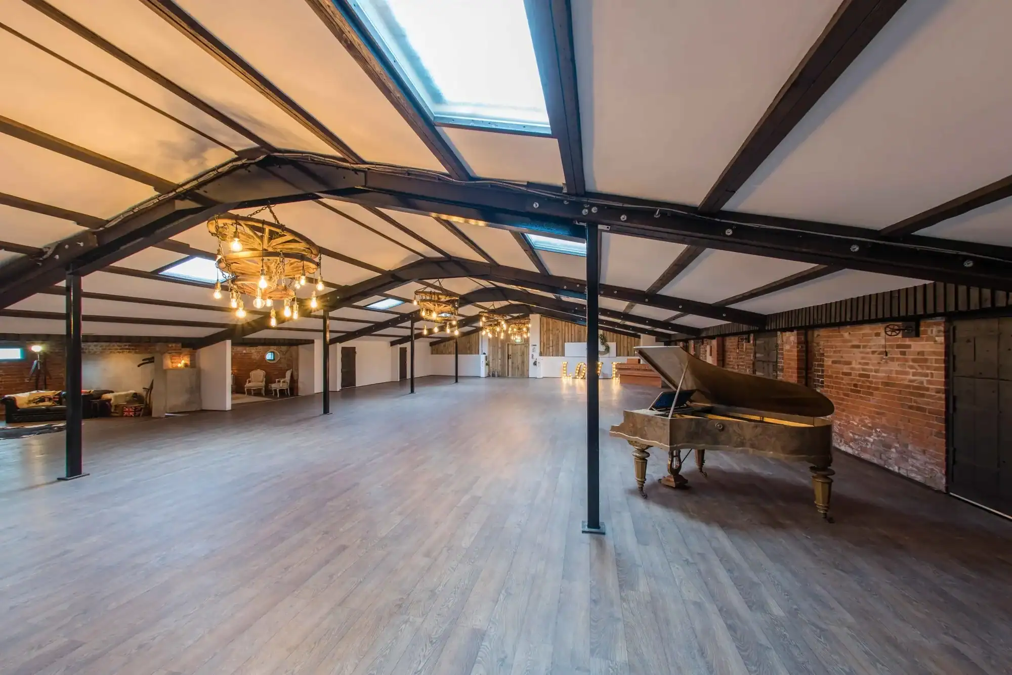 Spacious Loft with Exposed Brick Walls and Skylights Interior view of a large loft featuring wooden floors, brick walls, skylights, and elegant chandelie.