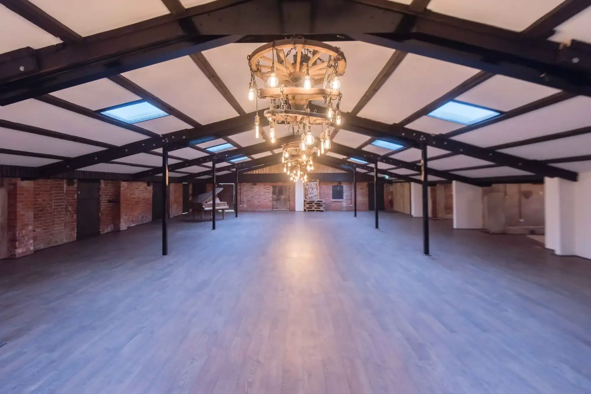 Spacious loft with exposed brick walls and elegant lighting fixtures. Large open-plan loft with brick walls, wooden flooring, and vintage chandeliers.