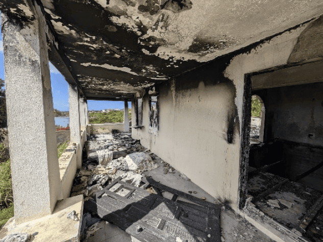 Fire-damaged house interior with charred walls and debris in Fortlands, Basseterre, Saint Kitts.