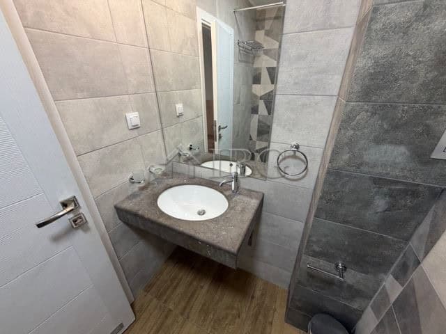 Bathroom with gray tiled walls and a white sink in a contemporary apartment.