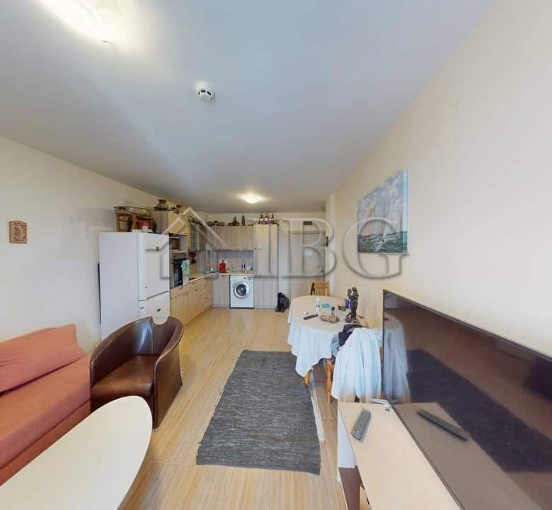 Interior view of a living room with sofa, TV, and kitchen in Kosharitsa apartment complex.