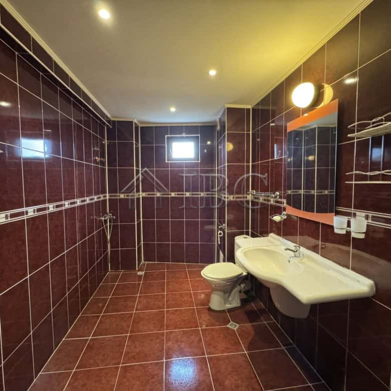 Modern bathroom featuring dark tiled walls and floor, with a white sink, toilet, and ample lighting.