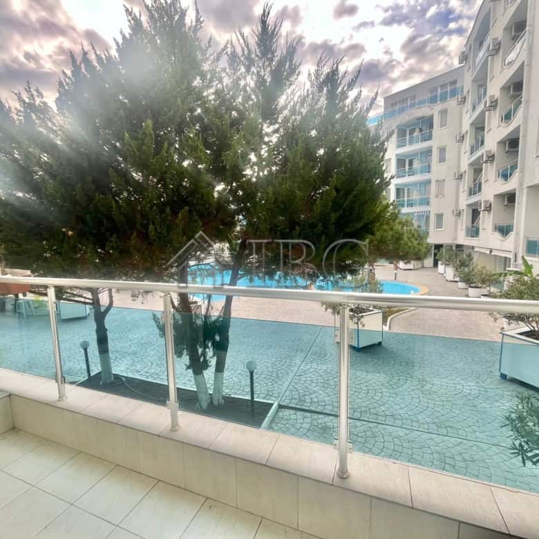 Pool view from a studio apartment balcony in Odyssey, Nessebar. Modern building with pool and lush g.