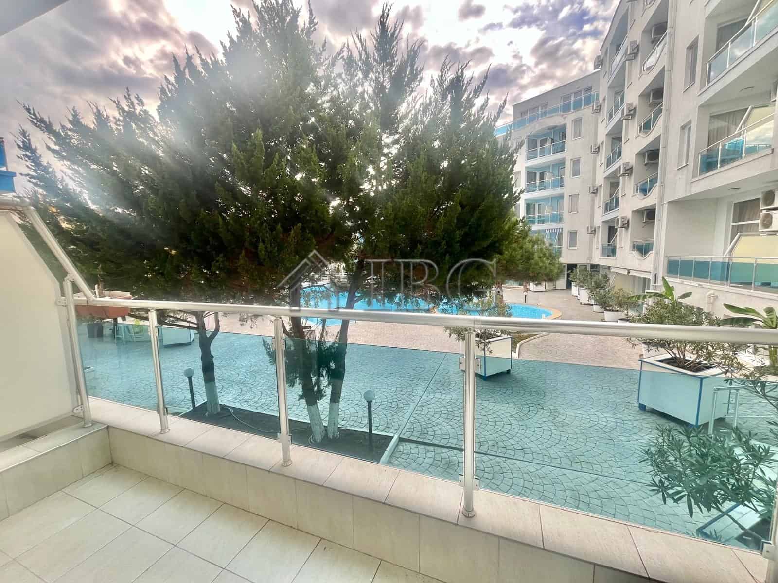 Pool view from a studio apartment balcony in Odyssey, Nessebar. Modern building with pool and lush g.