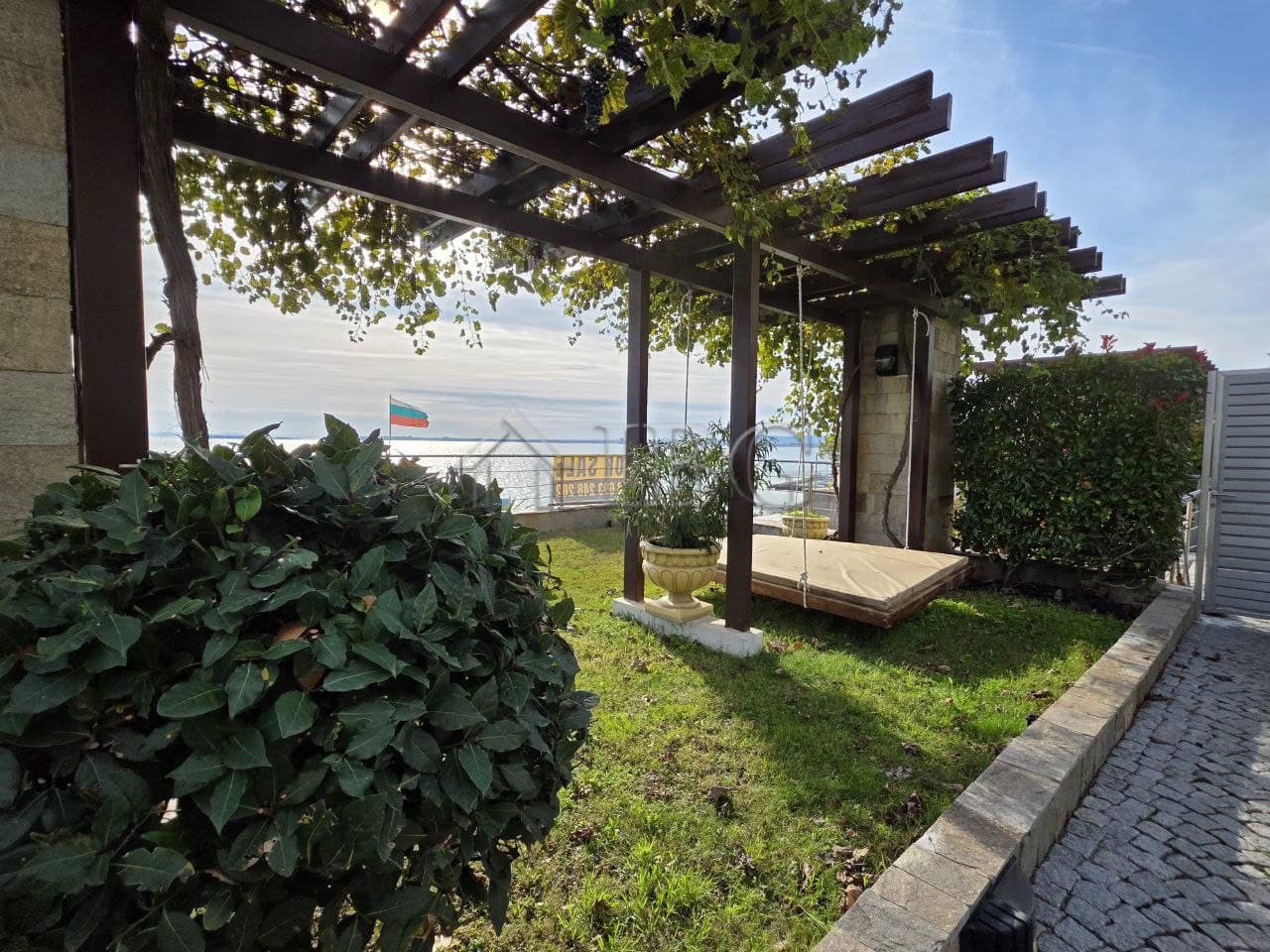 Sea view balcony of a 1-bedroom apartment in Sveti Vlas, Bulgaria, with outdoor seating and lush gre.