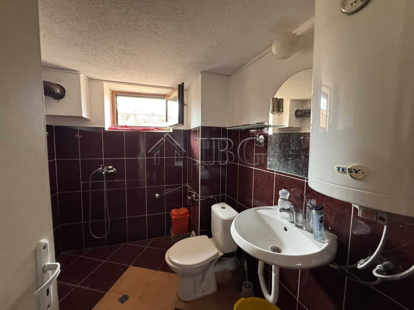 Modern bathroom with shower, toilet, and sink in Kosharitsa property. Bright window offers natural l.