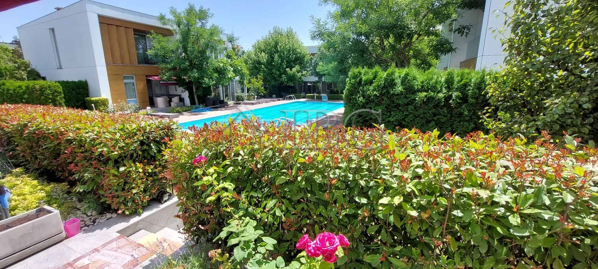 Bright outdoor pool area surrounded by lush greenery and colorful flowers in Sarafovo.
