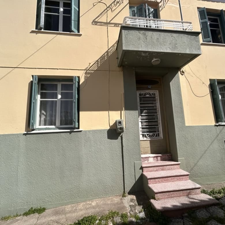 Apt building with yellow exterior, green shutters, and entrance stairs.