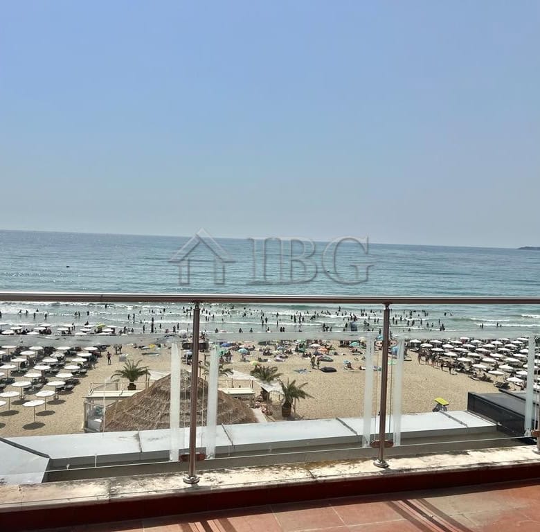 Oceanfront property with sandy beach, sunbeds, and clear blue sea.