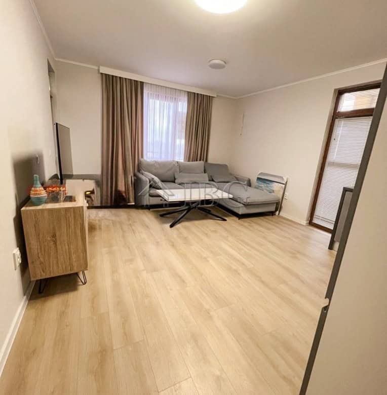 Bright living room with sofa and large window in a fully furnished 1-bedroom apartment.