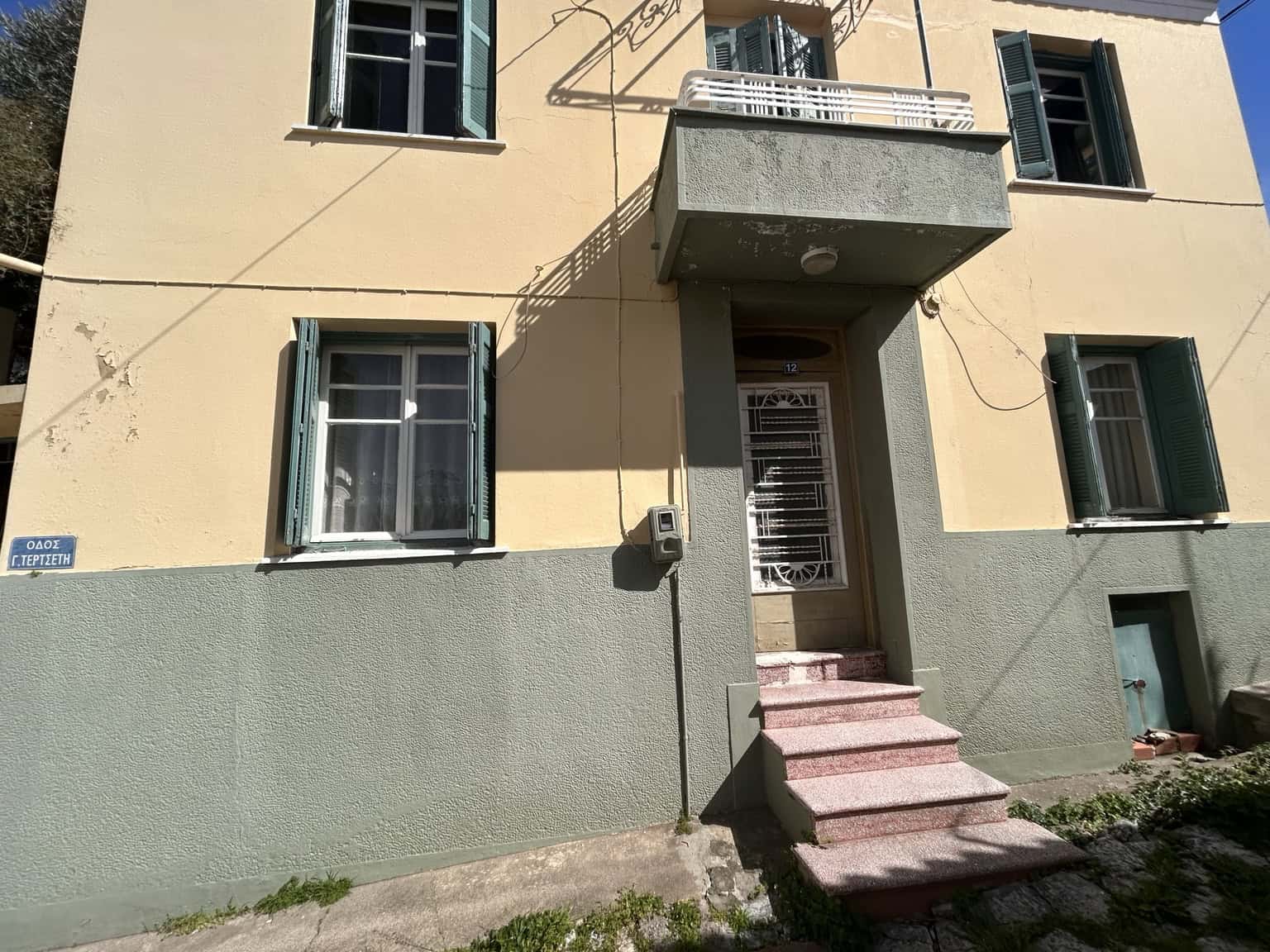 Apt building with yellow exterior, green shutters, and entrance stairs.