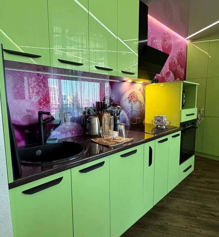 Bright green kitchen cabinets with black handles and vibrant pink and yellow accents.