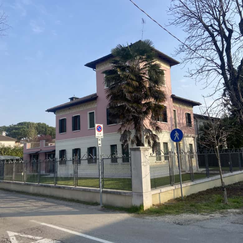 Elegant pink villa with lush garden and tall palm tree in a quiet neighborhood.